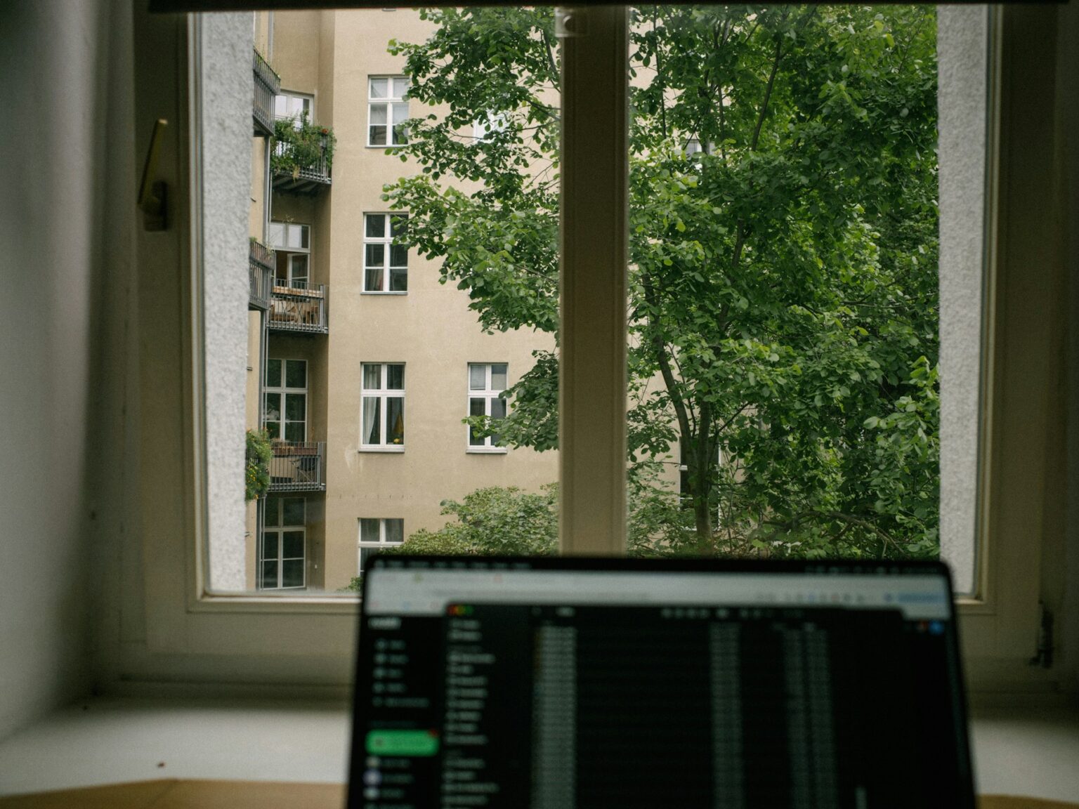 Laptop workspace overlooking a leafy city apartment building