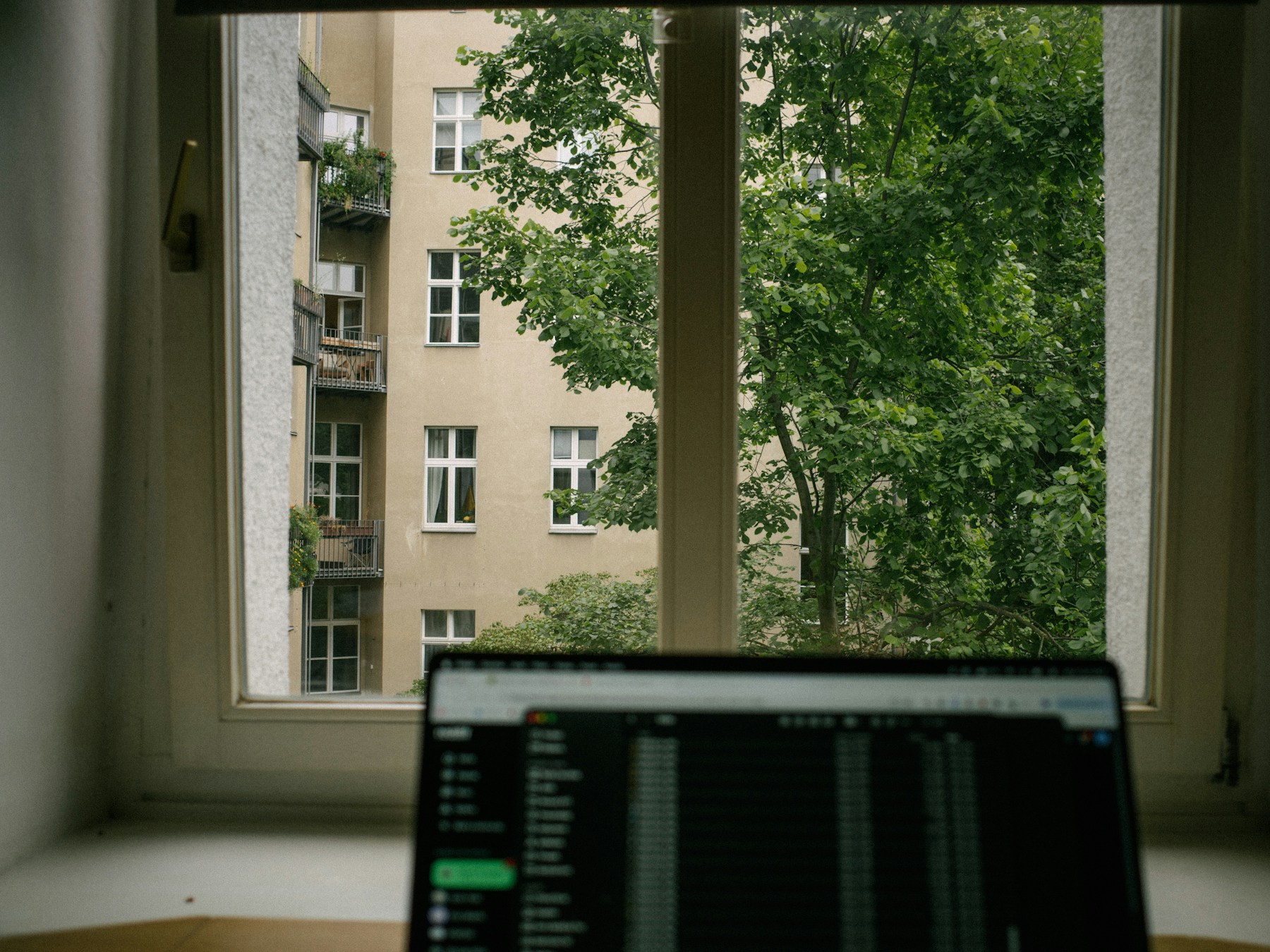 Laptop workspace overlooking a leafy city apartment building