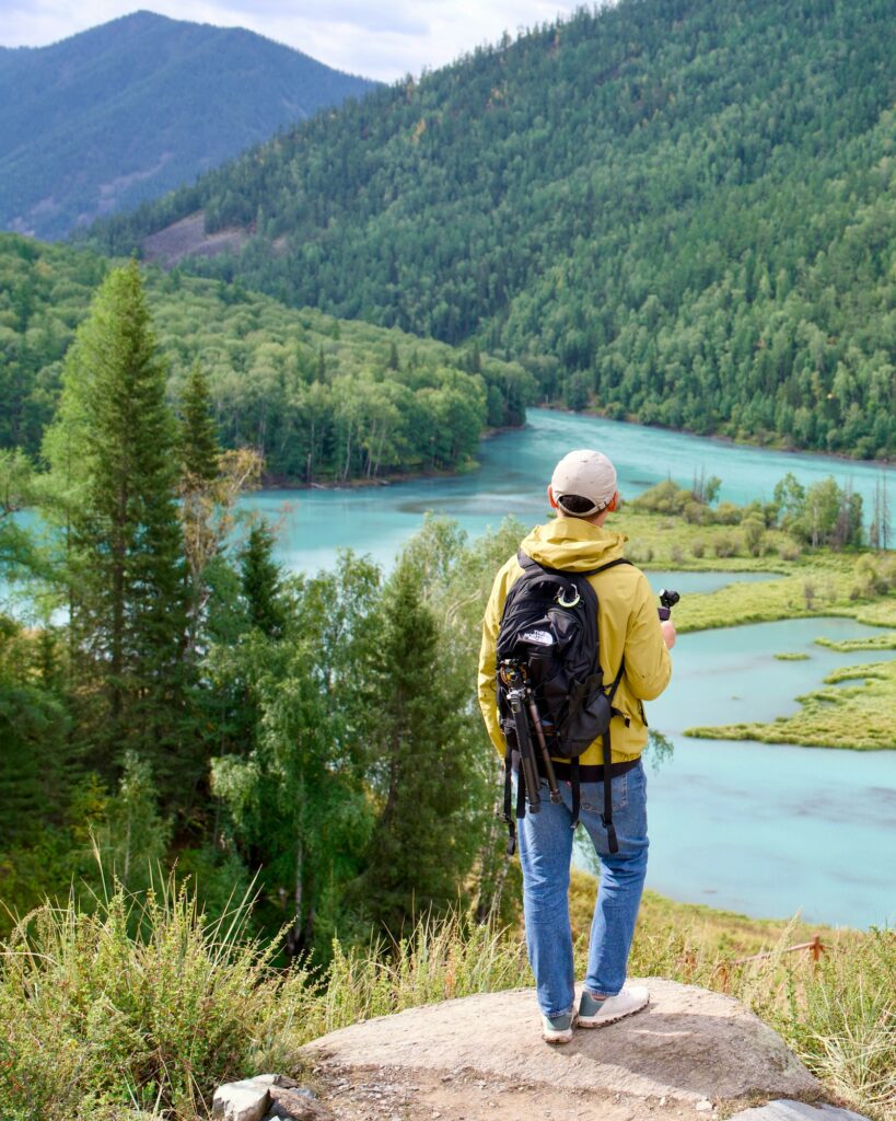 Solo traveler with a backpack looking across a turquoise river and forest